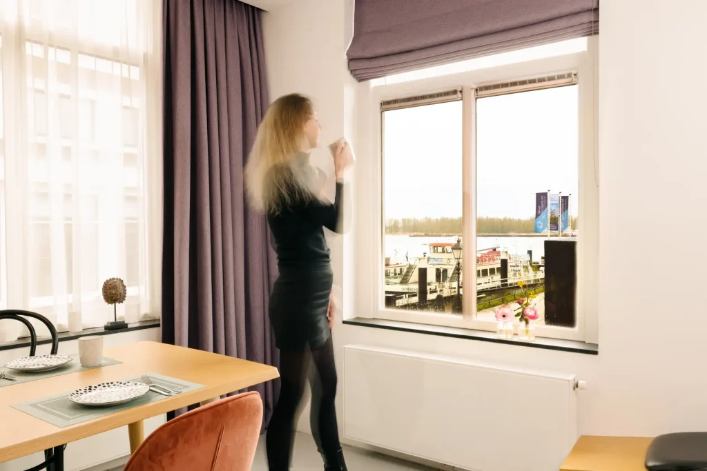 Model kijkt uit raam met uitzicht Buiten de Waterpoort longstay suite 15 hotel Goud en Zilver